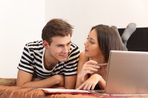 Couple (lying on bed) with laptop in front of them